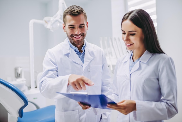 Portrait of smiling dentist and assistant looking at clipboard in modern dental clinic
