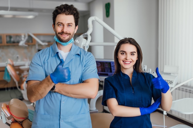 Portrait of smiling dentist standing with arms crossed with her colleague, showing okay sign.
