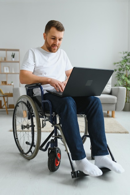 휠체어에 앉아 집에서 노트북 작업을 하는 웃고 있는 장애인 남성의 초상화 특별한 도움이 필요한 프리랜서와 장애인 개념을 가진 젊은 노동자