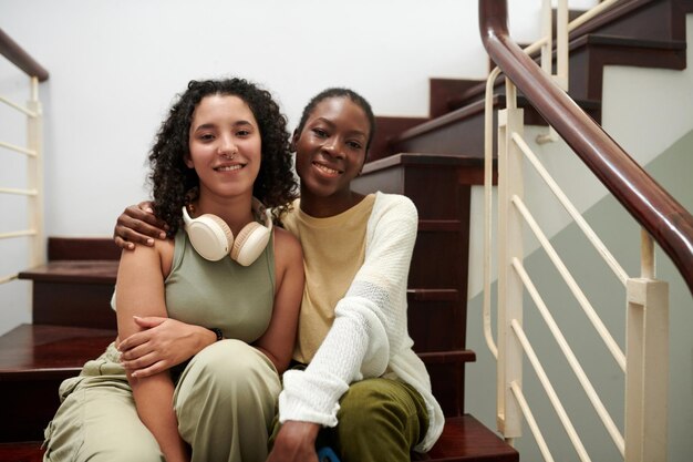 Portrait of smiling diverse friends sitting on steps smiling at looking at camera