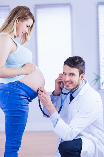 Portrait of smiling doctor examining stomach of standing pregnant patient