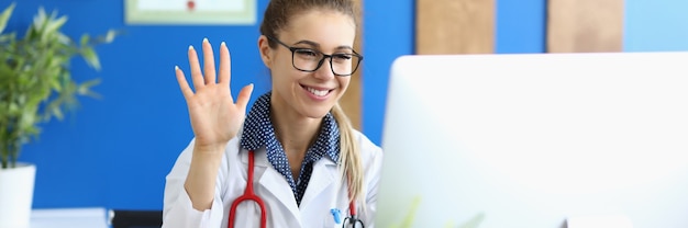 Ritratto di medico sorridente saluto e agitando la mano. professionista che fornisce consulenza online. signora che guarda il computer con gioia. concetto di sanità e medicina online