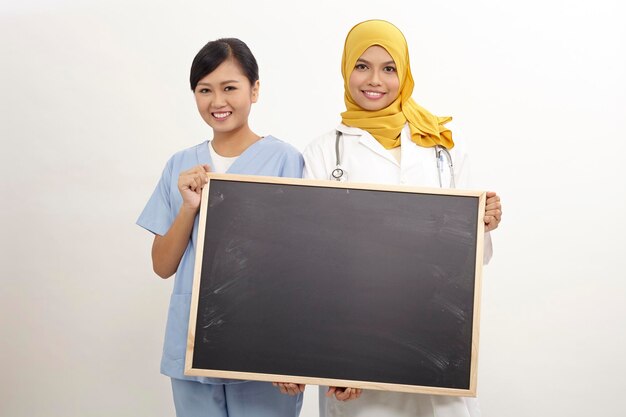 Portrait of smiling doctor and nurse holding blank blackboard while standing against white background