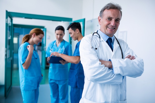 Portrait of smiling doctor standing with arms crossed in corridor