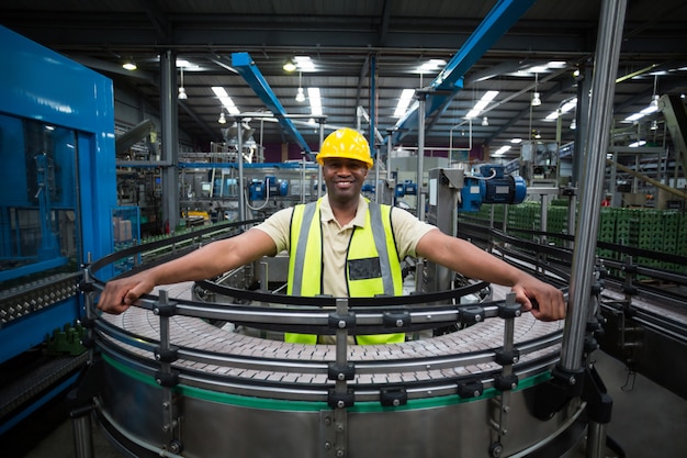 Portrait of smiling factory worker standing near the conveyor belt in factory