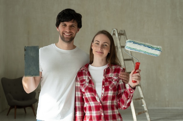 Photo portrait smiling family couple holding paint roller and brush young couple doing home repairs