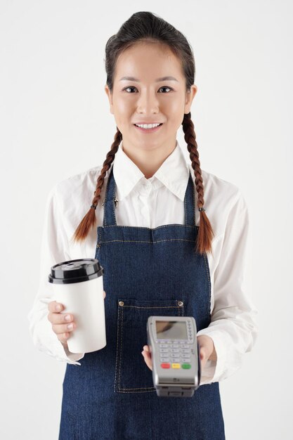 Portrait of smiling female barista giving cup of takeout coffee and payment terminal