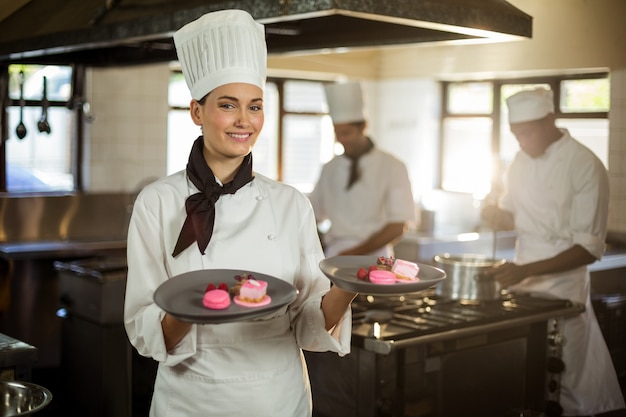 Ritratto del cuoco unico femminile sorridente che presenta i piatti di dessert