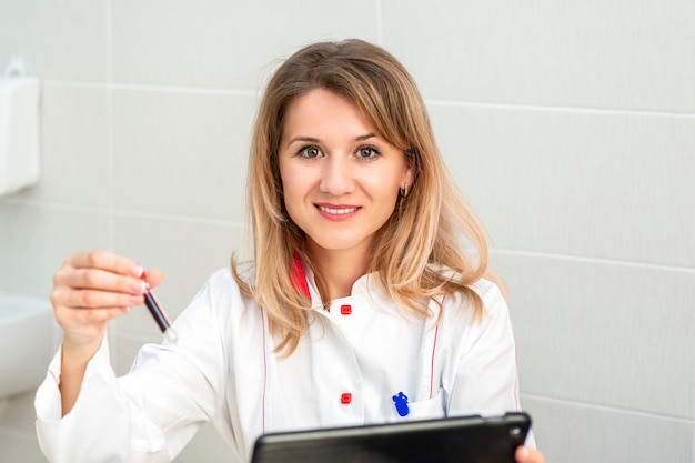 Portrait of smiling female doctor or nurse holds test tube with blood. concept of good analysis