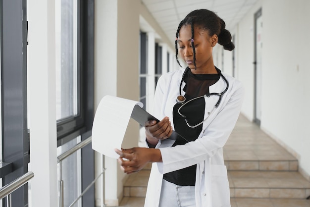 Портрет улыбающейся женщины-врача в скрабах в больничном коридоре с цифровым планшетом