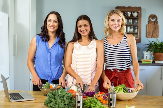 Ritratto degli amici femminili sorridenti che preparano alimento in cucina