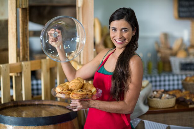 Portrait of smiling female staff holding a tray of snacks at counter