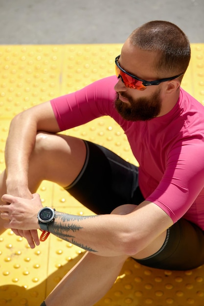 Portrait of a smiling fitness man resting while sitting on a ground at the track field outdoors