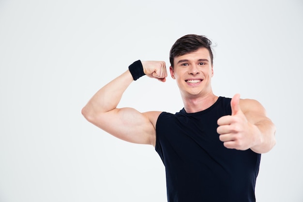 Portrait of a smiling fitness man showing his biceps and thumb up isolated