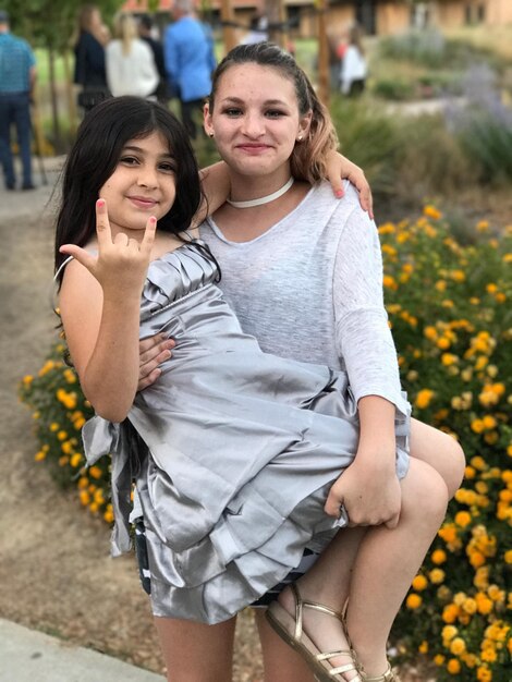 Photo portrait of smiling girl carrying gesturing sister outdoors