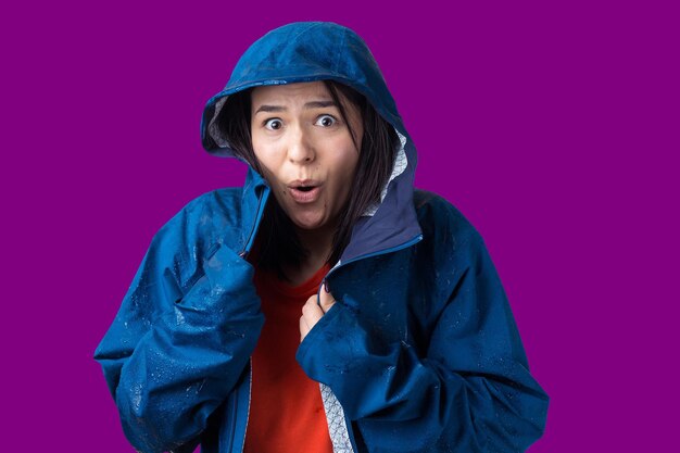 Portrait of a smiling girl dressed in blue raincoat in drops posing with hood on grey background in a studio