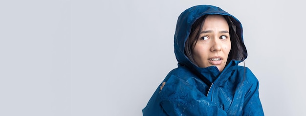 Portrait of a smiling girl dressed in blue raincoat in drops posing with hood on grey