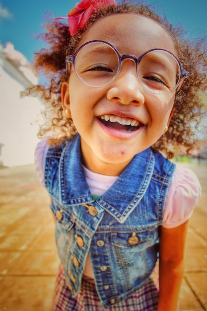 portrait of smiling girl in eyeglasses standing on footpath
