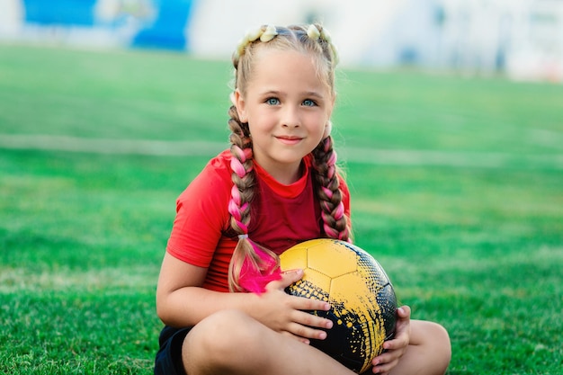 Ritratto di giocatore di football ragazza sorridente con pallone da calcio seduto sull'erba