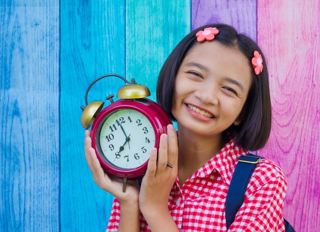 Portrait of smiling girl holding alarm clock while standing against fence