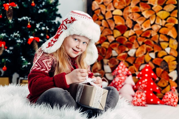 Photo portrait of smiling girl holding christmas present while sitting on fur at home