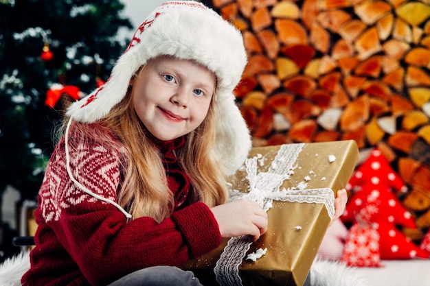 Портрет улыбающейся девушки с рождественским подарком, сидящей дома на мехо.