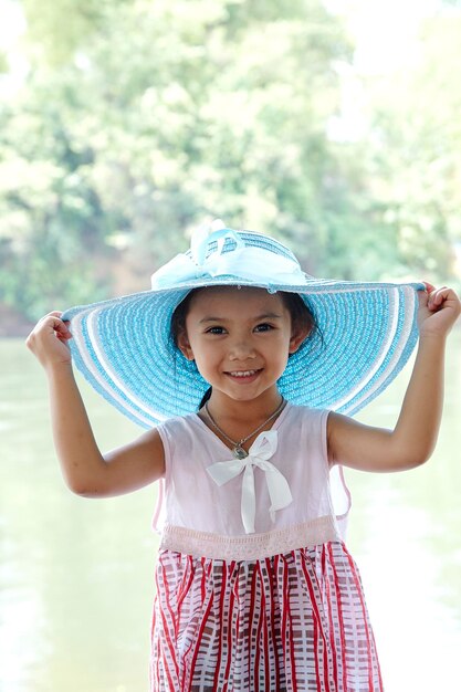 Portrait of smiling girl holding hat while standing against lake