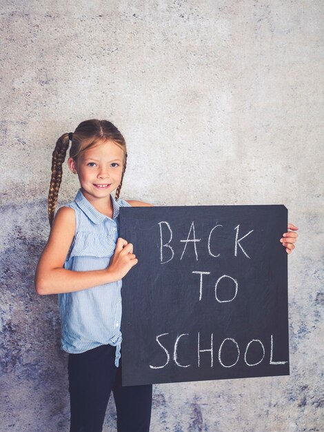 Photo portrait of smiling girl holding writing slate with text against wall