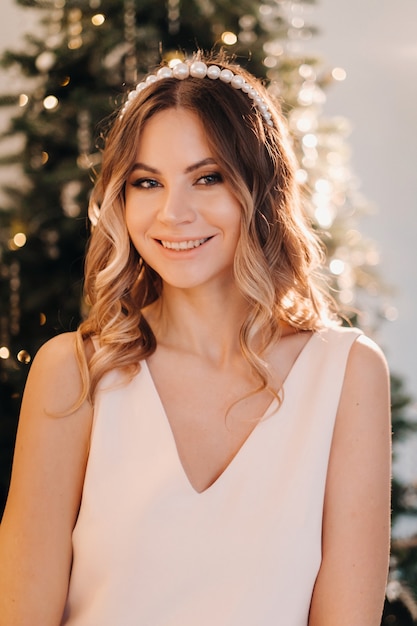 Portrait of a smiling girl in a pink dress near the Christmas tree at home.