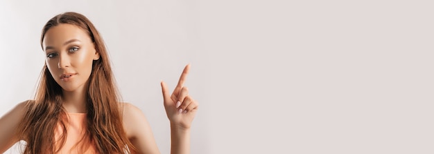 Portrait of a smiling girl pointing finger to the side at on a white isolated background. Positive woman points to an idea, a place for advertising