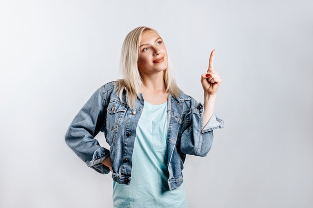 Portrait of a smiling girl pointing finger up at copyspace isolated. A woman points to an idea, a place for advertising. Positive blonde.