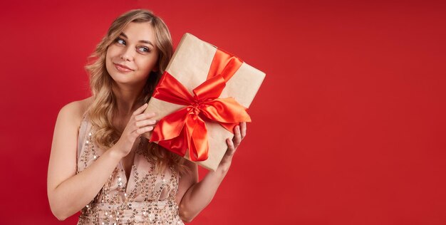 Portrait of a smiling girl receiving a gift for the holiday on a red background