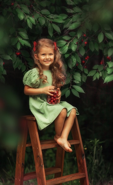 Photo portrait of smiling girl sitting and eating cherries
