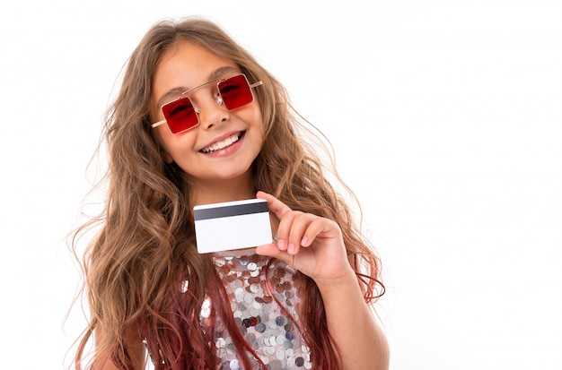 Portrait of smiling girl in square red sunglasses holding plastic bank card isolated