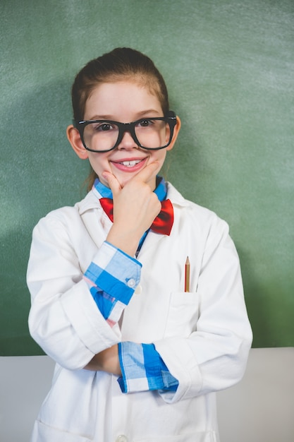 Portrait of smiling girl standing with hand on chin in classroom