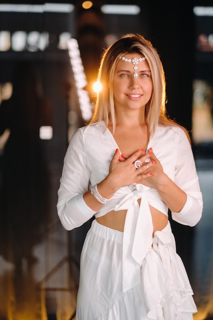 Portrait of a smiling girl in a white dress with her palms clasped in front of her