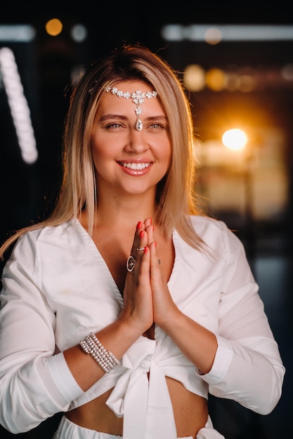 Foto ritratto di una ragazza sorridente in abito bianco con i palmi delle mani giunte davanti a lei