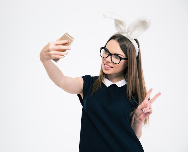 Portrait of a smiling girl with bunny ears making selfie photo on smartphone isolated