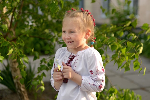 Portrait of a smiling girl with a flower in a Ukrainian embroidered shirt Kid's emotions from happy