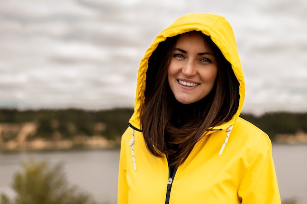 Ritratto di ragazza sorridente con impermeabile con cappuccio giallo sul lago