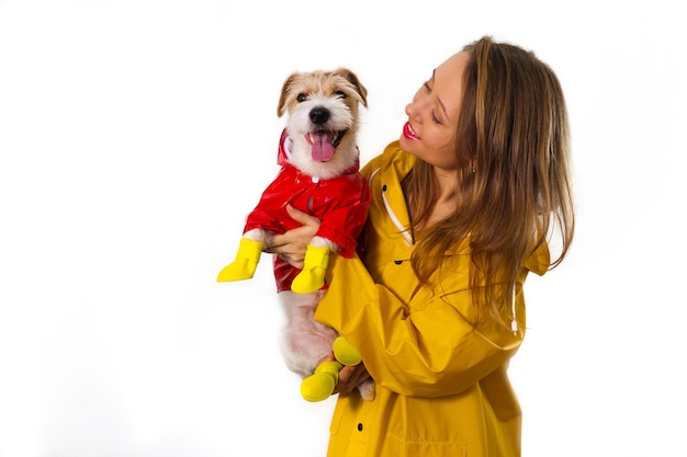 彼女の腕に赤いジャケットを着た犬ジャックラッセルテリアと黄色のレインコートで笑顔の女の子の肖像画。白い背景に分離
