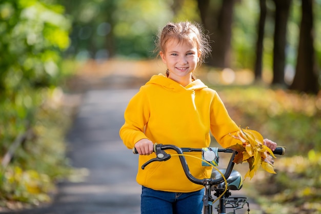 秋の公園で自転車と黄色のスウェットシャツの笑顔の女の子の肖像画