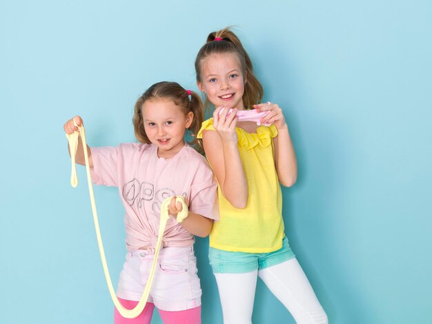 Portrait of smiling girls playing with slime against blue background