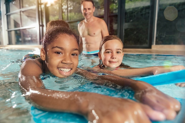 Портрет улыбающихся девушек с инструктором, практикующих в крытом бассейне