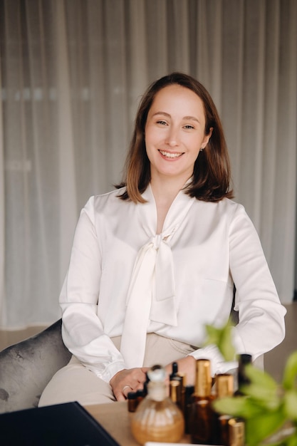 Portrait of a smiling girlwoman sitting in an armchair An aromatherapist in a white blouse is sitting in the office