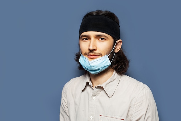 Portrait of smiling guy wearing medical face mask on background of blue color.