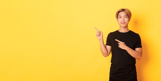 Portrait of smiling handsome asian man in black tshirt pointing fingers upper left corner showing lo...