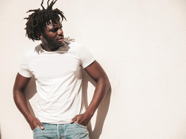 Portrait of smiling handsome hipster modelUnshaven African man dressed in white summer tshirt and jeans Fashion male with dreadlocks hairstyle posing on the street background