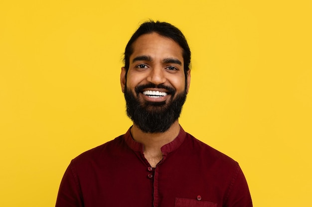 Portrait of smiling handsome young indian man posing on yellow