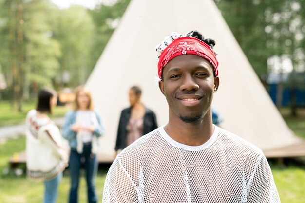 Portrait of smiling handsome young man with beard wearing red bandana spending time at festival campsite